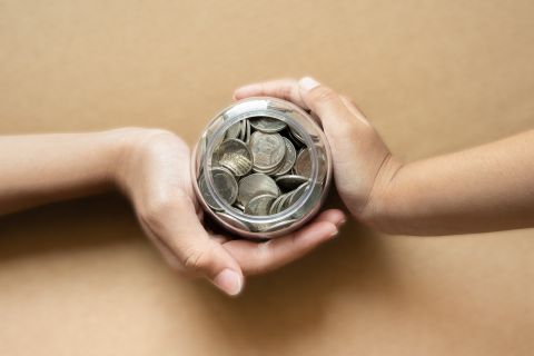 Kid hands holding coins in a jar together as saving concept for family or education