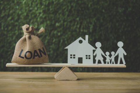 paper house and paper cut family balancing on swing with money bag with loan inscription on green